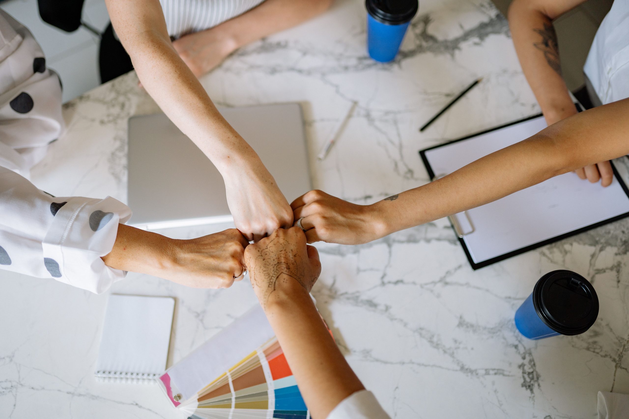 Top view of diverse team members fist bumping over a marble table in a collaborative office setting.
